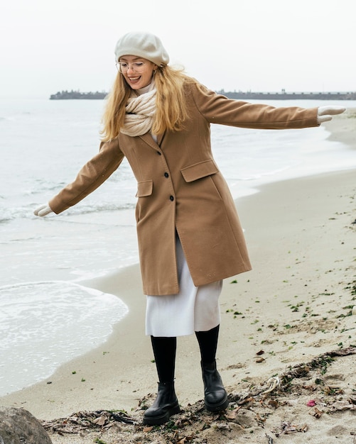 Vooraanzicht van smileyvrouw met wanten op het strand tijdens de winter