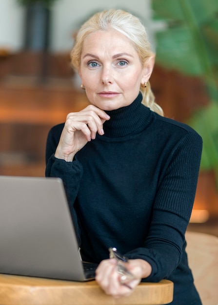 Gratis foto vooraanzicht van stoïcijnse oudere vrouw met zonnebril poseren tijdens het werken op laptop