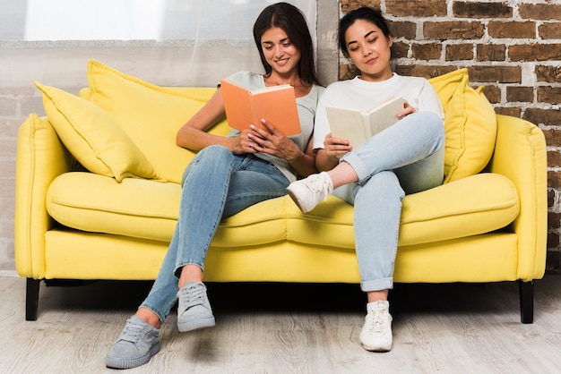 Vooraanzicht van twee vrienden die thuis op bank met boeken ontspannen