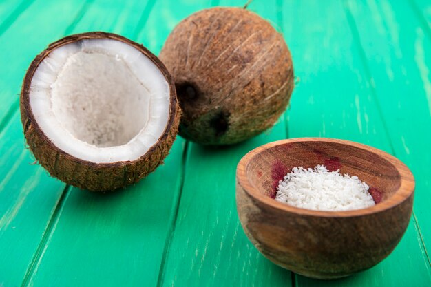 Vooraanzicht van verse kokosnoten met kokos poeder op een houten kom op groene ondergrond
