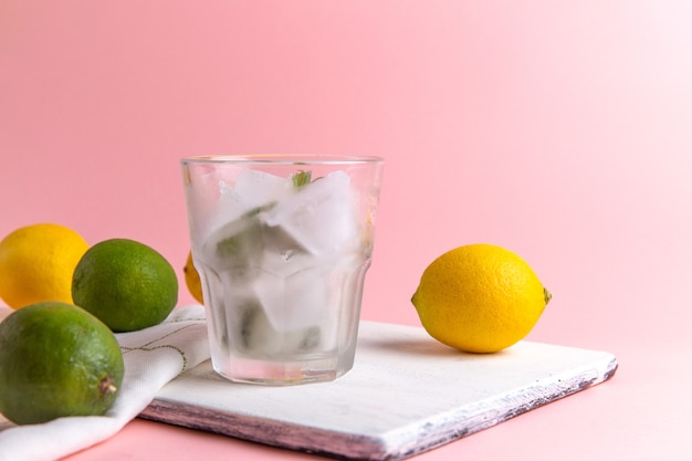 Vooraanzicht van verse koude limonade met ijs in glas samen met verse citroenen op de roze muur