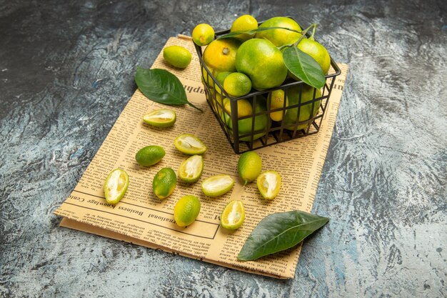 Vooraanzicht van verse kumquats en citroenen in een zwarte mand op kranten op grijze achtergrond stock afbeelding