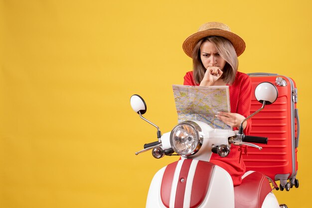 Vooraanzicht van verward mooi meisje op bromfiets met rode koffer met kaart