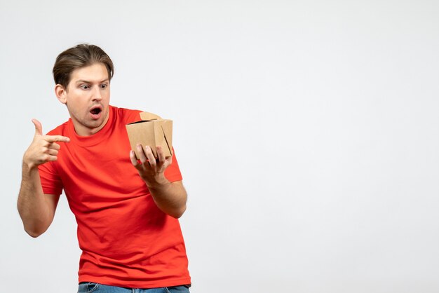 Vooraanzicht van verwarde emotionele jonge kerel in rode blouse die kleine doos op witte achtergrond richt