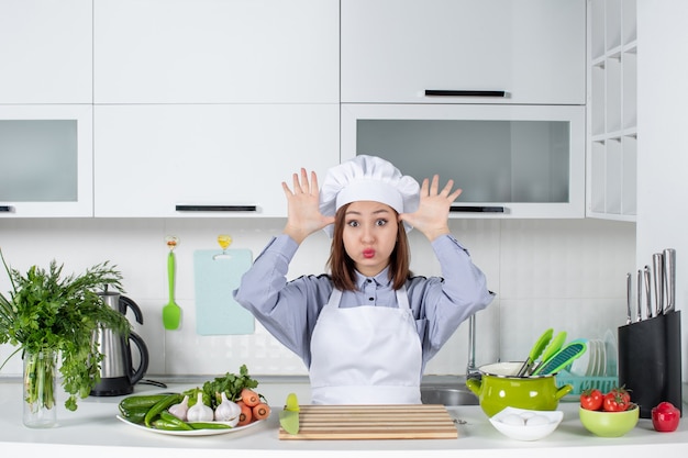 Vooraanzicht van verwarde en emotionele vrouwelijke chef-kok en verse groenten poseren voor de camera in de witte keuken