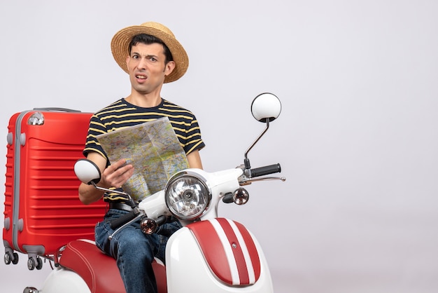 Vooraanzicht van verwarde jonge man met strooien hoed op bromfiets bedrijf kaart