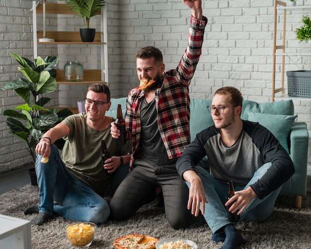 Vooraanzicht van vrolijke mannelijke vrienden die op tv naar sport kijken en pizza hebben