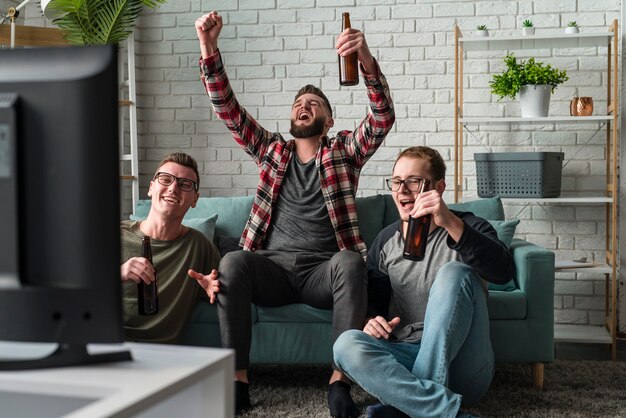 Vooraanzicht van vrolijke mannelijke vrienden die op tv naar sport kijken