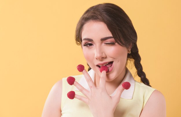 Vooraanzicht van vrouw frambozen eten uit haar vingertoppen en knipogen
