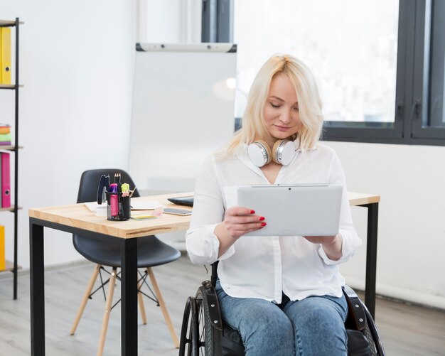 Vooraanzicht van vrouw in rolstoel op de tablet van de bureauholding
