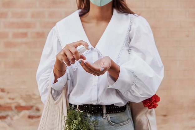 Gratis foto vooraanzicht van vrouw met gezichtsmasker die handdesinfecterend middel gebruikt