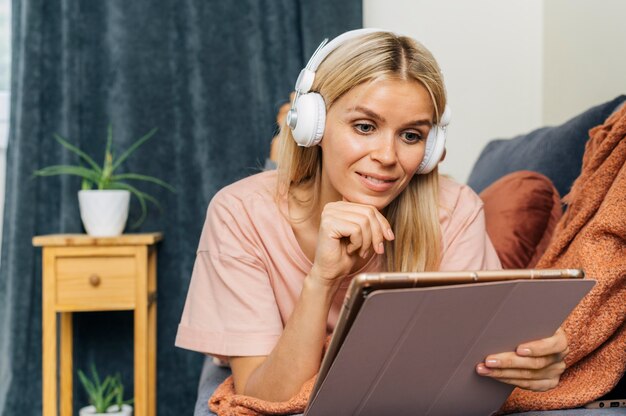 Vooraanzicht van vrouw thuis op Bank met behulp van tablet met koptelefoon