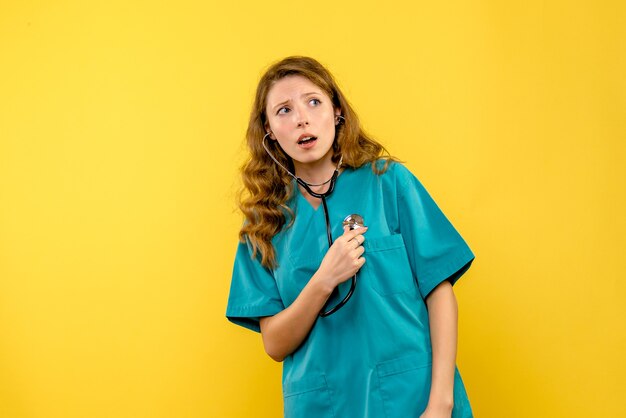 Vooraanzicht van vrouwelijke arts die stethoscoop op gele muur met behulp van