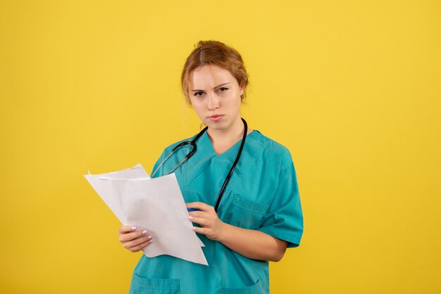 Vooraanzicht van vrouwelijke arts in de analyse van de medische kostuumholding op gele muur