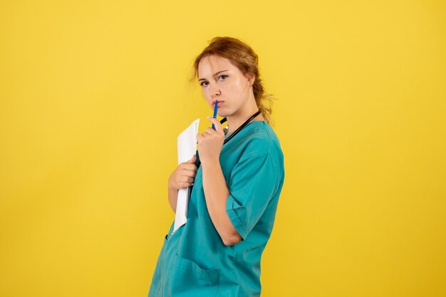 Vooraanzicht van vrouwelijke arts in de analyse van de medische kostuumholding op gele muur