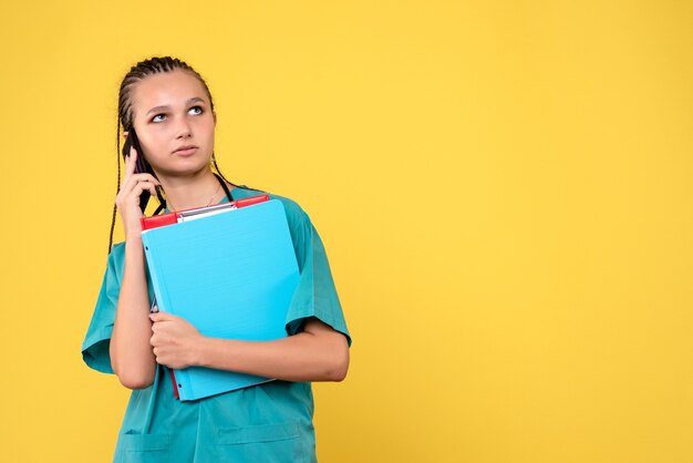 Vooraanzicht van vrouwelijke arts in medisch kostuum die op telefoon op gele muur spreken