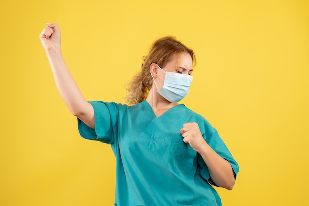 Vooraanzicht van vrouwelijke arts in medisch kostuum en masker op gele muur