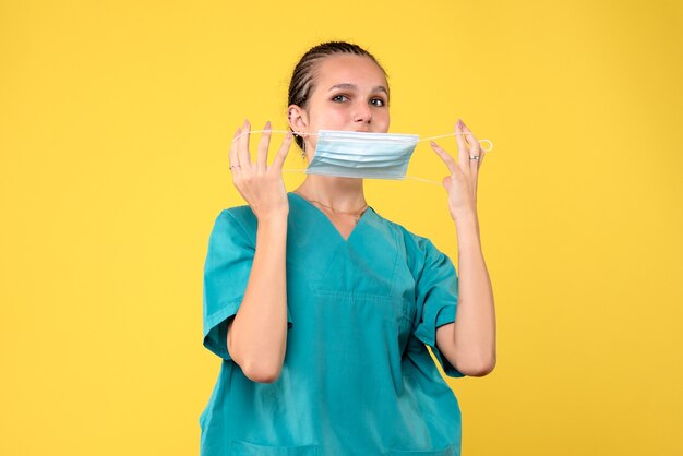 Vooraanzicht van vrouwelijke arts in medisch kostuum en steriel masker op gele muur