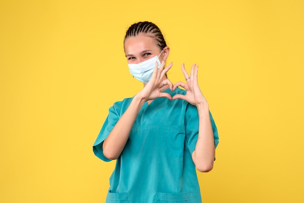 Vooraanzicht van vrouwelijke arts in medisch kostuum en steriel masker op gele muur