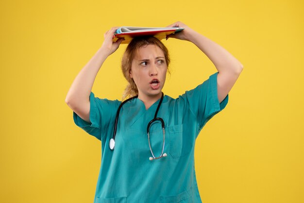 Vooraanzicht van vrouwelijke arts in medisch kostuum met analyse op gele muur