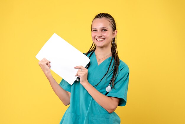 Vooraanzicht van vrouwelijke arts in medisch kostuum met documenten op gele muur