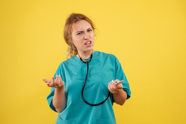 Vooraanzicht van vrouwelijke arts in medisch kostuum met stethoscoop die op gele muur wordt verward