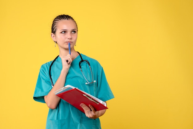 Vooraanzicht van vrouwelijke arts in medisch kostuum met verschillende analyse op gele muur