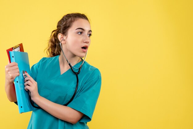 Vooraanzicht van vrouwelijke arts in medisch overhemd met stethoscoop op gele muur