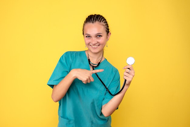 Vooraanzicht van vrouwelijke arts in medisch overhemd met stethoscoop op gele muur