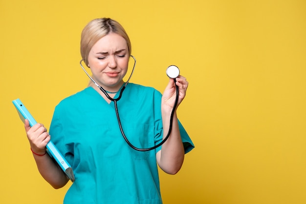 Vooraanzicht van vrouwelijke arts met analyse en stethoscoop op gele muur