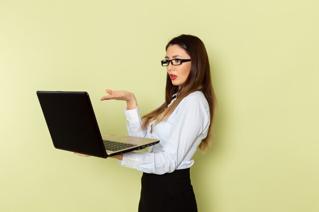 Vooraanzicht van vrouwelijke beambte in wit overhemd en zwarte rok die haar laptop op groene muur houdt