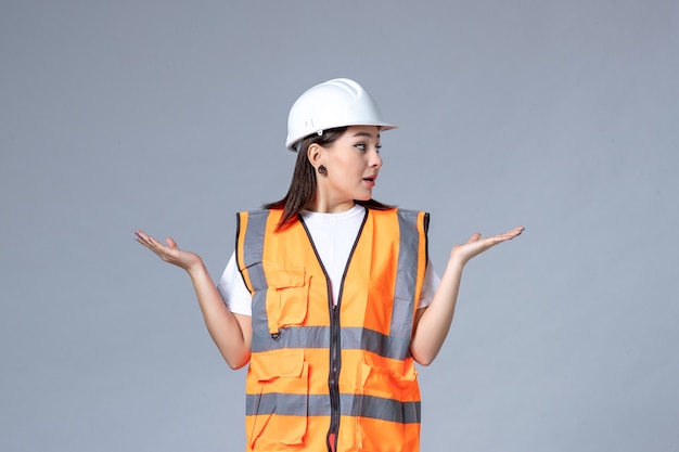 Vooraanzicht van vrouwelijke bouwer in uniforme en beschermende helm op grijze muur