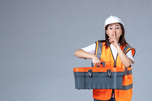 Vooraanzicht van vrouwelijke bouwer met zware gereedschapskoffer op witte muur Gratis Foto