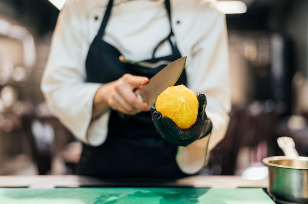 Vooraanzicht van vrouwelijke chef-kok die sinaasappel snijdt