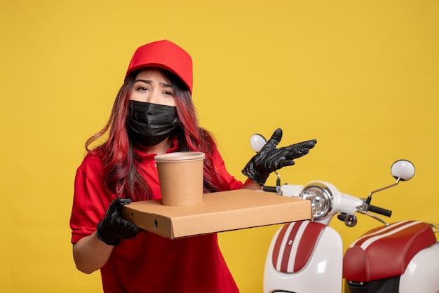 Vooraanzicht van vrouwelijke koerier in masker met leveringsvoedsel op gele muur