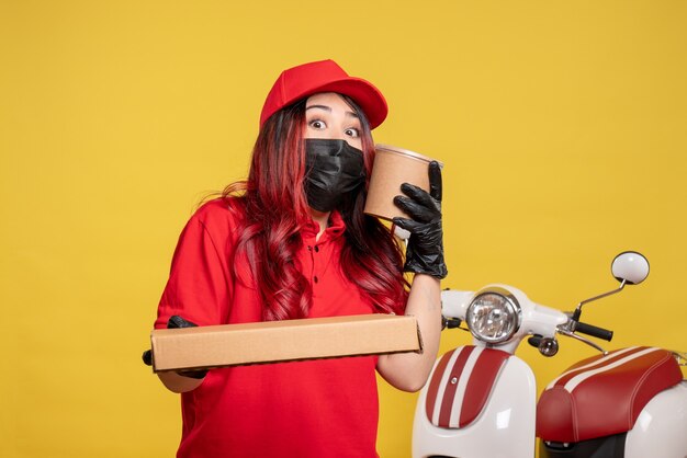 Vooraanzicht van vrouwelijke koerier in masker met leveringsvoedsel op gele muur