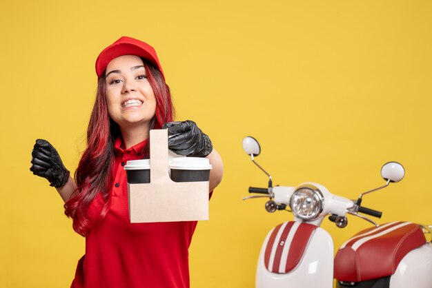 Vooraanzicht van vrouwelijke koerier in rood uniform met koffie op gele muur