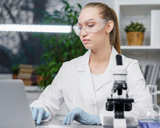 Gratis foto vooraanzicht van vrouwelijke onderzoeker in het laboratorium met veiligheidsbril en microscoop