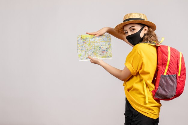 Vooraanzicht van vrouwelijke reiziger die met zwart masker kaart op witte muur steunt