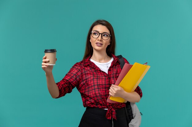 Vooraanzicht van vrouwelijke student die de dossiers en de koffie van de rugzakholding op de blauwe muur draagt