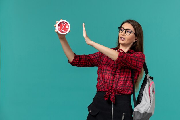 Gratis foto vooraanzicht van vrouwelijke student die de klokken van de rugzakholding op de blauwe muur draagt