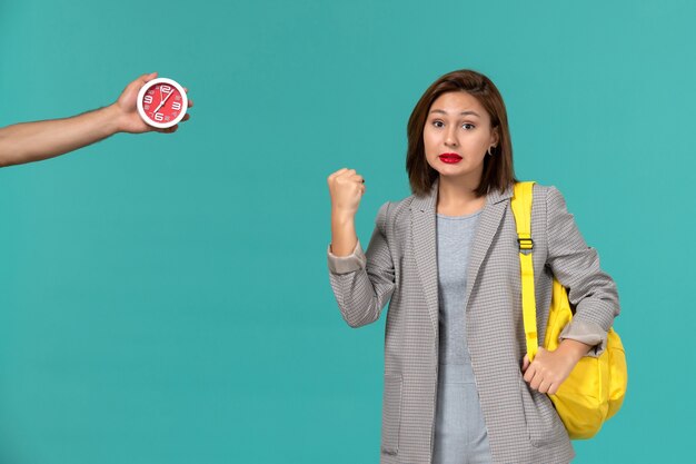 Vooraanzicht van vrouwelijke student in grijs jasje gele rugzak dragen op blauwe muur