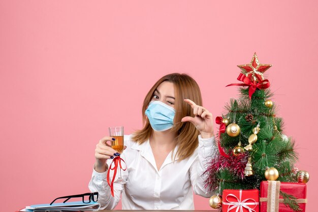 Vooraanzicht van vrouwelijke werknemer in steriel masker Kerstmis vieren met champagne op roze