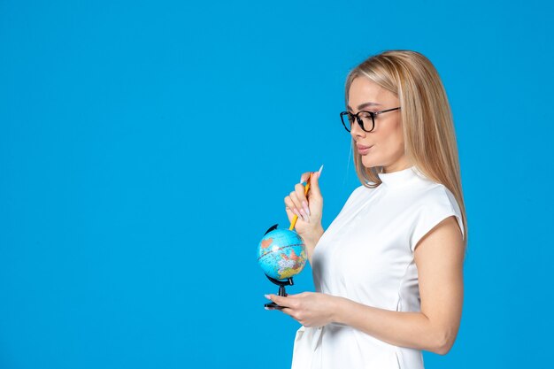 Vooraanzicht van vrouwelijke werknemer in witte jurk met kleine aardebol op blauwe muur