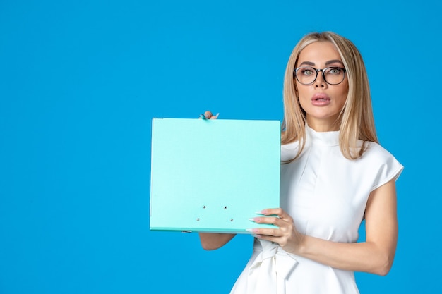 Vooraanzicht van vrouwelijke werknemer in witte jurk met map op blauwe muur