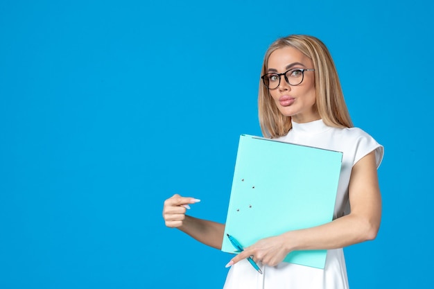 Vooraanzicht van vrouwelijke werknemer in witte jurk met map op blauwe muur