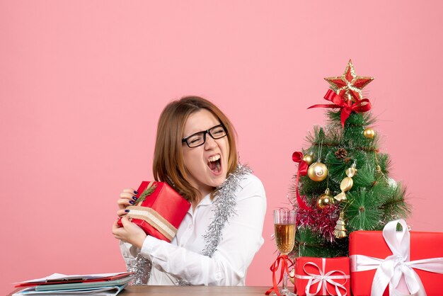 Vooraanzicht van vrouwelijke werknemer zittend rond kerstcadeautjes en boom op roze