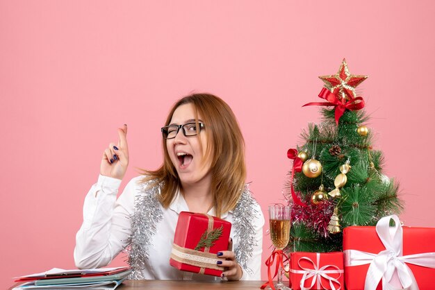 Vooraanzicht van vrouwelijke werknemer zittend rond kerstcadeautjes en boom op roze