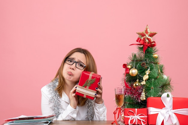 Vooraanzicht van vrouwelijke werknemer zittend rond kerstcadeautjes en boom op roze