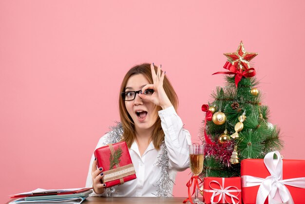 Vooraanzicht van vrouwelijke werknemer zittend rond kerstcadeautjes en boom op roze